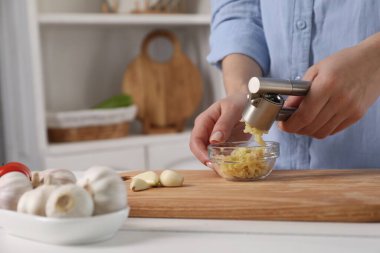 Mutfaktaki beyaz ahşap masada sarımsak sıkan kadın, yakın plan.