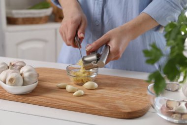 Mutfaktaki beyaz ahşap masada sarımsak sıkan kadın, yakın plan.