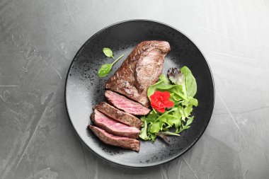 Lezzetli ızgara et parçaları ve gri masada yeşiller, üst manzara.