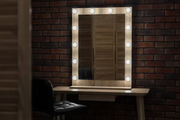 Mirror with light bulbs, table and chair in makeup room