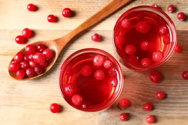 Tasty cranberry juice in glasses and fresh berries on wooden table, flat lay