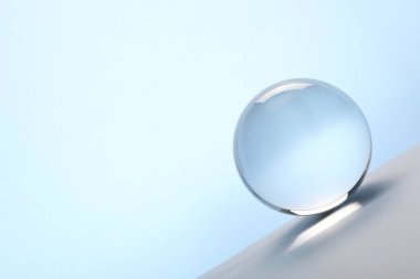 Masanın üzerinde açık mavi arka plana karşı şeffaf cam top. Metin için boşluk