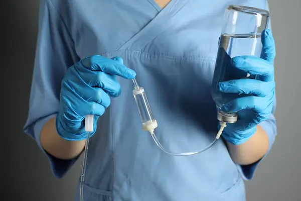 Nurse with IV infusion set on grey background, closeup