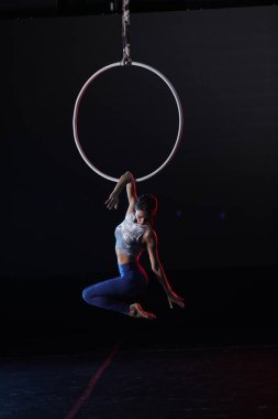 Genç bir kadın, arka planda hava halkası üzerinde akrobatik hareketler yapıyor.