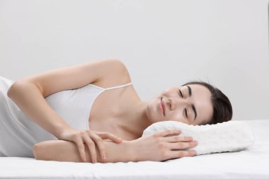 Açık gri arka planda ortopedik yastıkta uyuyan kadın