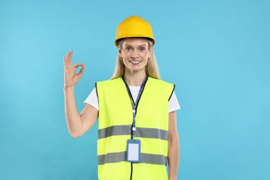 Sert şapkalı ve rozetli mühendis açık mavi arka planda iyi bir hareket gösteriyor.