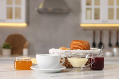 Kahvaltı mutfakta servis edilir. Taze kruvasan, kahve, reçel, bal ve beyaz masada tatlandırılmış süt.