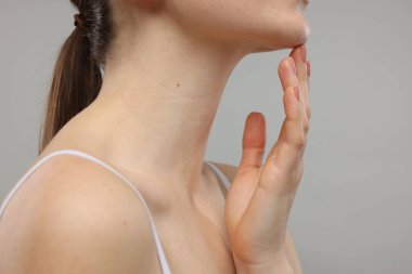 Gri arka planda çenesine dokunan kadın, yakın plan.