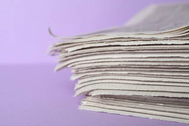 Açık mor arka planda gazete yığını, yakın plan. Gazeteci işi.