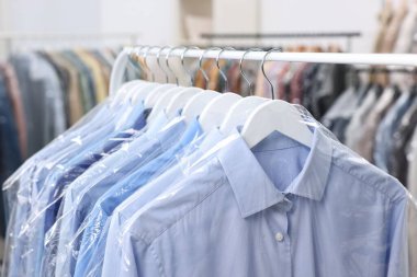 Kuru temizleme servisi. Plastik poşetlerdeki birçok farklı giysi kapalı yerlerde asılı, yakın plan.