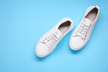 Açık mavi arka planda bir çift şık beyaz spor ayakkabı, üst manzara. Metin için boşluk