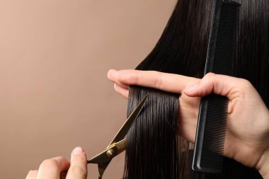 Kuaför açık kahverengi arka planda müşterinin saçını makasla kesiyor, yakın plan. Metin için boşluk