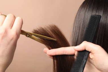 Kuaför, bej arka planda makasla müşterinin saçını kesiyor.