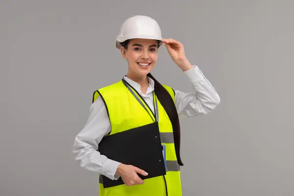 Engineer in hard hat holding clipboard on grey background
