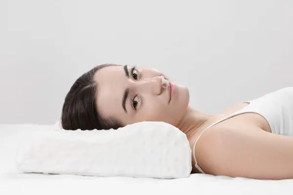 Woman lying on orthopedic pillow against light grey background