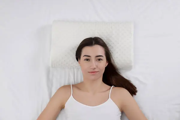 Woman lying on orthopedic pillow in bed, top view