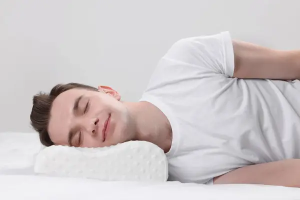 Man sleeping on orthopedic pillow against light grey background