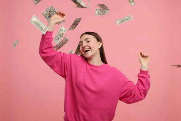 Happy woman under money shower on pink background