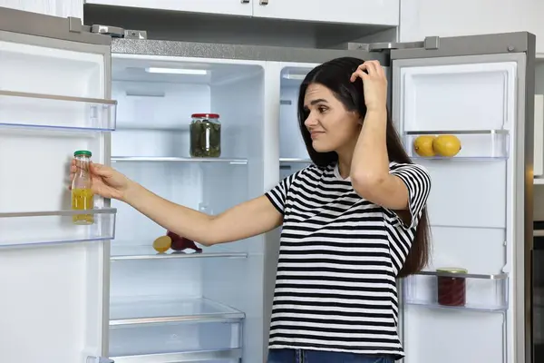 Upset woman near empty refrigerator in kitchen
