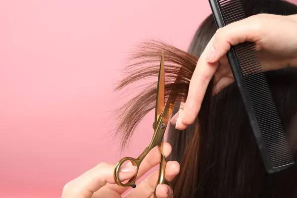Hairdresser cutting client\'s hair with scissors on pink background, closeup. Space for text