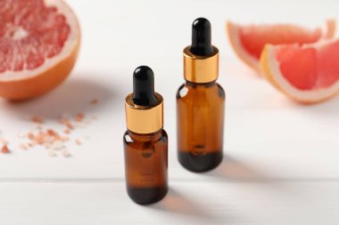 Beyaz ahşap masadaki şişelerde greyfurt yağı, yakın plan.