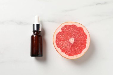 Şişede greyfurt yağı ve beyaz mermer masa üzerinde yarım meyve.
