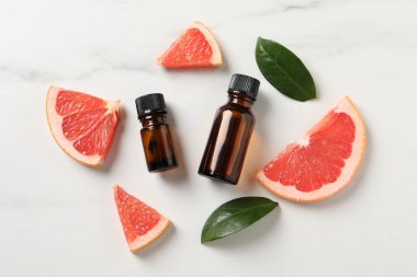 Şişelerde greyfurt yağı, yapraklar ve beyaz mermer masa üzerinde meyve kesimi, düz yatıyordu.