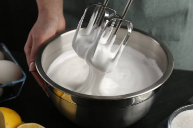 Siyah masada el çırpıcı ile krem şanti yapan kadın, yakın plan.