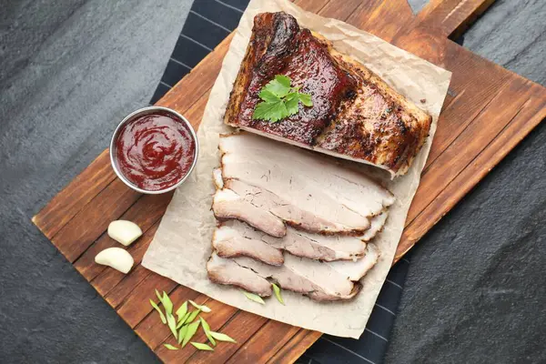 Soslu fırında domuz göbeği ve siyah desenli masanda maydanoz.