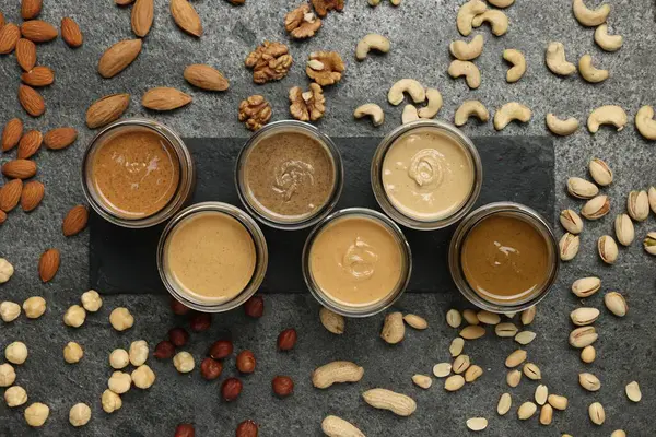 Kavanozlarda lezzetli fındık ezmesi ve gri masada çiğ fındık, düz yatıyordu.