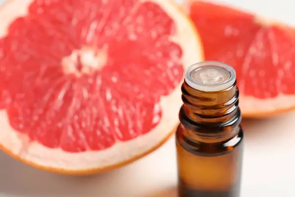 Grapefruit essential oil in bottle and fruit on white table, closeup. Space for text