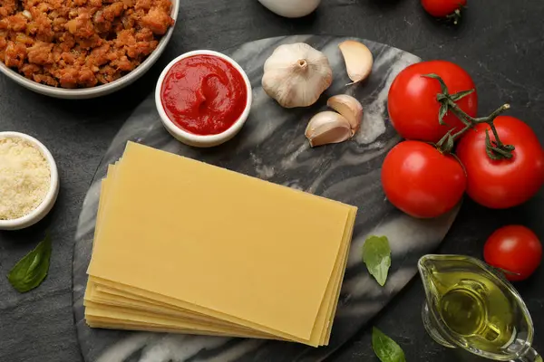 Flat lay composition with products for cooking lasagna on dark textured table