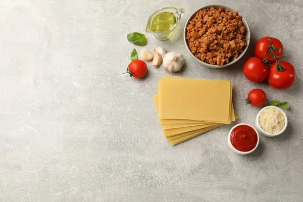 Flat lay composition with products for cooking lasagna on grey textured table. Space for text