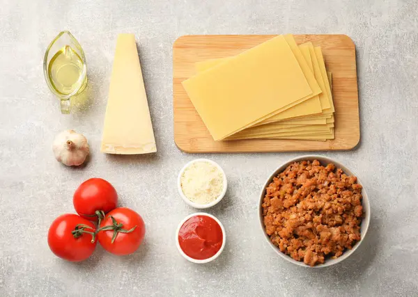 Flat lay composition with products for cooking lasagna on grey textured table