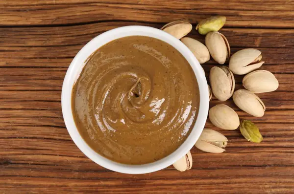 Lezzetli fındık ezmesi kasede ve ahşap masada fıstıklar, üst manzara.