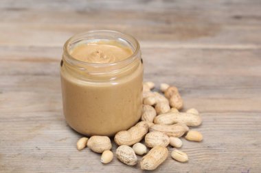 Kavanozda lezzetli fındık ezmesi ve ahşap masada fıstık, yakın plan.