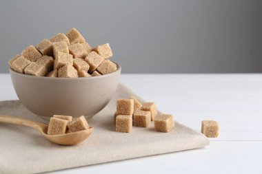 Brown sugar cubes on white wooden table, space for text