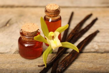 Aromatik vanilya özü, kapsüller ve çiçek ahşap masada, yakın plan.