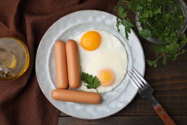 Lezzetli haşlanmış sosisler ve ahşap masada servis edilen sahanda yumurtalar.