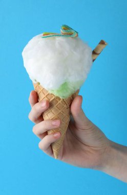 Açık mavi arka planda pamuk şekerli waffle külahı tutan kadın, yakın plan.