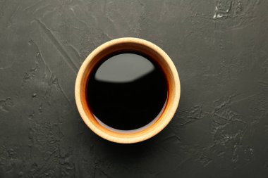 Ahşap kasede soya sosu, siyah desenli masa, üst manzara.