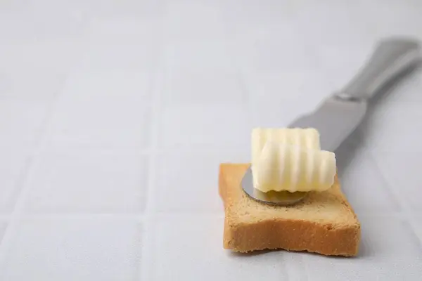 Tasty butter curl, knife and piece of dry bread on white tiled table, closeup. Space for text