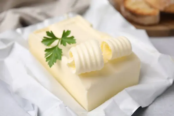 Tasty butter with curl and parsley on light grey table, closeup