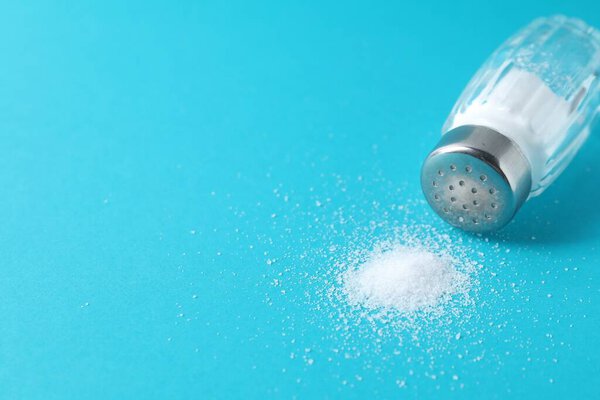 Organic white salt in glass shaker on light blue background, closeup. Space for text