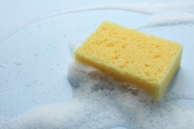 Açık mavi arka planda köpüklü sarı sünger, yakın plan