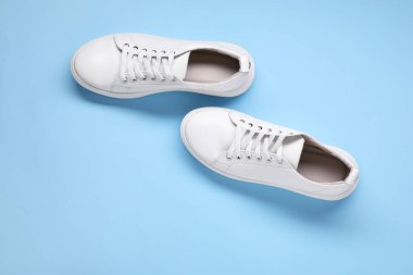 Açık mavi arka planda bir çift şık beyaz spor ayakkabı.