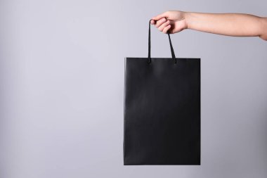 Gri arka planda kağıt alışveriş torbası tutan kadın, yakın plan. Metin için boşluk