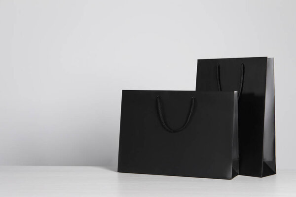 Black paper bags on white wooden table, space for text