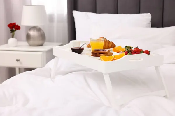 Tray with delicious breakfast on bed in room, closeup