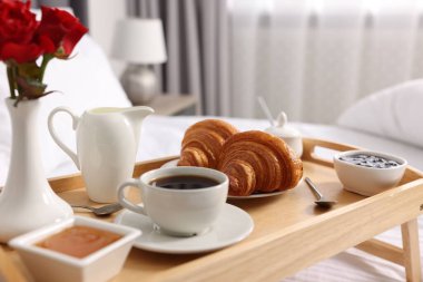 Yatakta servis edilen lezzetli kahvaltı. Taze kruvasanlar, kahve, reçel ve bal, ahşap tepside, yakın plan.